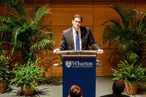 Ron Dermer talks at a Wharton podium with potted plants on the stage behind him