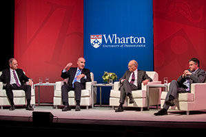 The Wharton Dean and three faculty members sit on a stage, in discussion