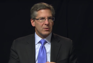 Headshot of Robert Moritz speaking in front of a black curtain