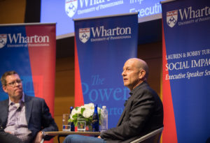 Bobby Turner and Chris Geczy in conversation on a stage surrounded by Wharton banners