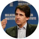 Headshot of a person in a suit gesturing while speaking, with a backdrop featuring the Milken Institute logo.