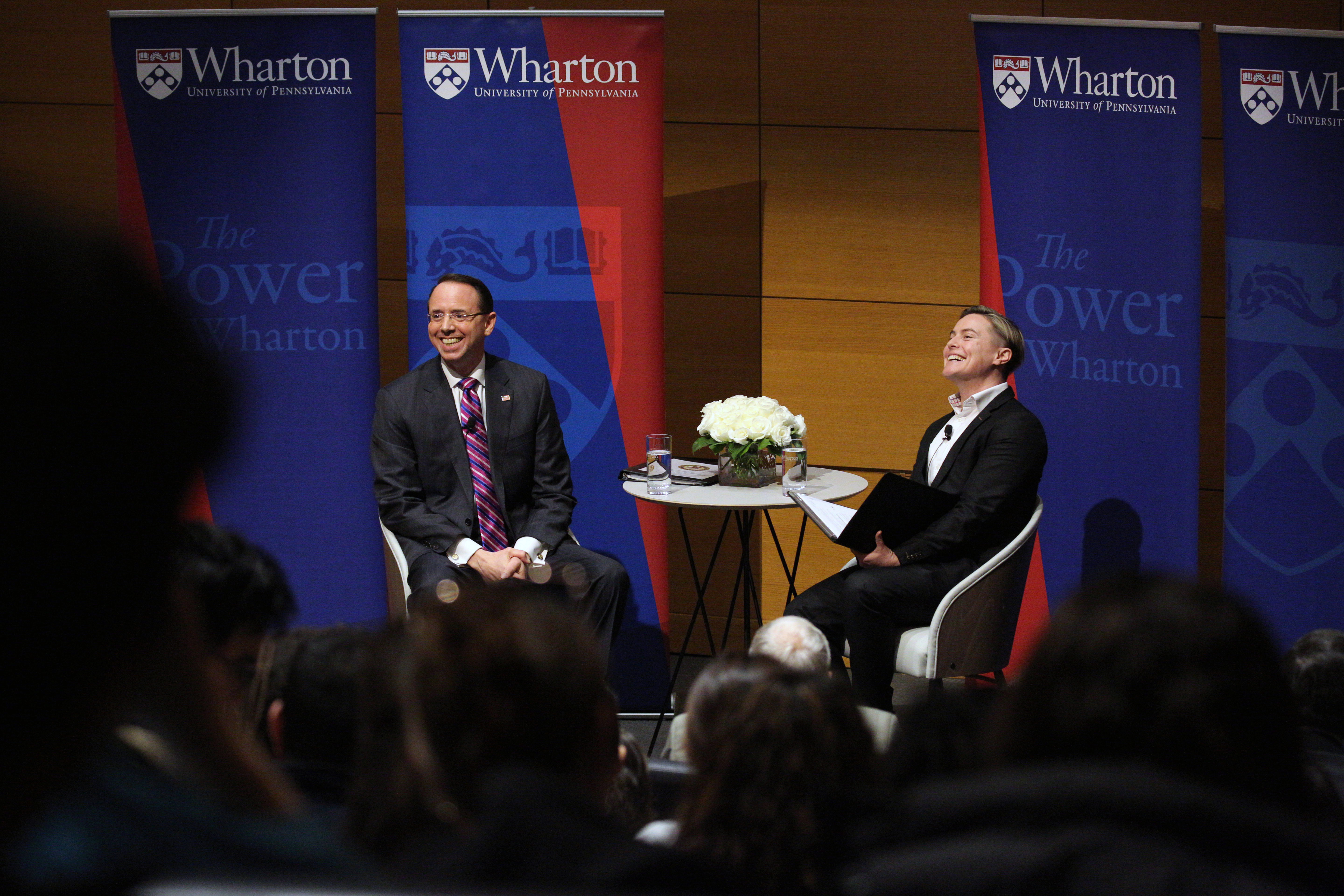 Rod Rosenstein and Amanda Shanor sit on stage, talking to an audience with Wharton signs behind them