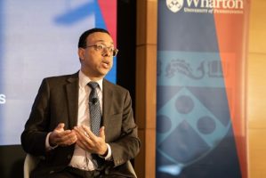 Wendell Pritchett sits on a stage, talking with a Wharton backdrop behind him